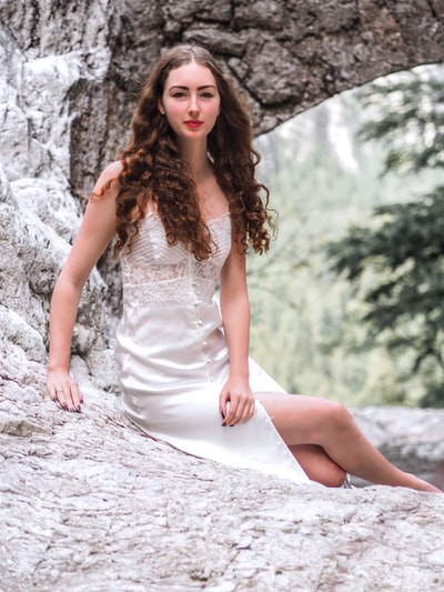 坐在岩石上的一位身穿白色纽扣连衣裙的微笑女子